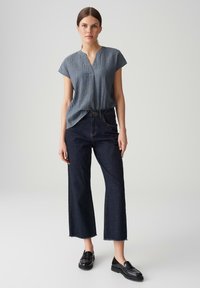 Top blu textured a maniche corte con scollatura a V, abbinato a jeans a vita alta blu scuro con gamba larga e mocassini neri.