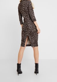 Kleid im Leopardenmuster mit figurbetonter Silhouette, knielangem Saum, seitlichen Schlitzen und Dreiviertelärmeln. Hergestellt aus einem glatten, dehnbaren Stoff.