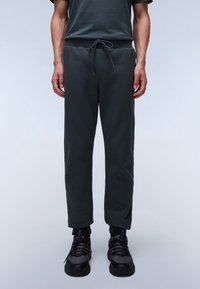 Donker groene joggerbroeken van zacht materiaal, met een elastische tailleband en een trekkoord, en taps toelopende pijpen. De schoenen zijn zwart met gestructureerde accenten.