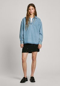 Světle modrý denimový pulover se zipovým límcem, oversized rukávy, kombinovaný s černou mini sukňou s náhodně rozmístěnými bílými akcenty. Černé mokasíny.