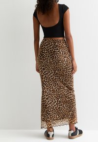 Maxi sukně s leopardím potiskem, volný design, průhledná látka a zvlněný lem; spárováno s černým upnutým topem a černými teniskami.