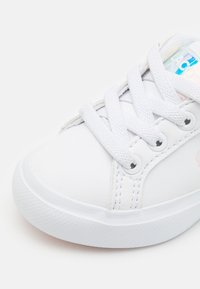 Baskets blanches en matériau synthétique lisse, avec des lacets plats, des œillets ronds et une semelle en caoutchouc texturée. Comprend un accent de logo subtil.