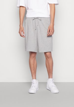 Shorts en coton gris avec une taille élastique et un lien de serrage. Coupe décontractée, longueur jusqu'aux genoux. Portés avec des baskets blanches montantes.