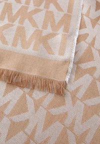 Beige mönstrad pläd med geometrisk design och fransar. Tygets textur är mjuk och vävd, med växlande färgtoner.
