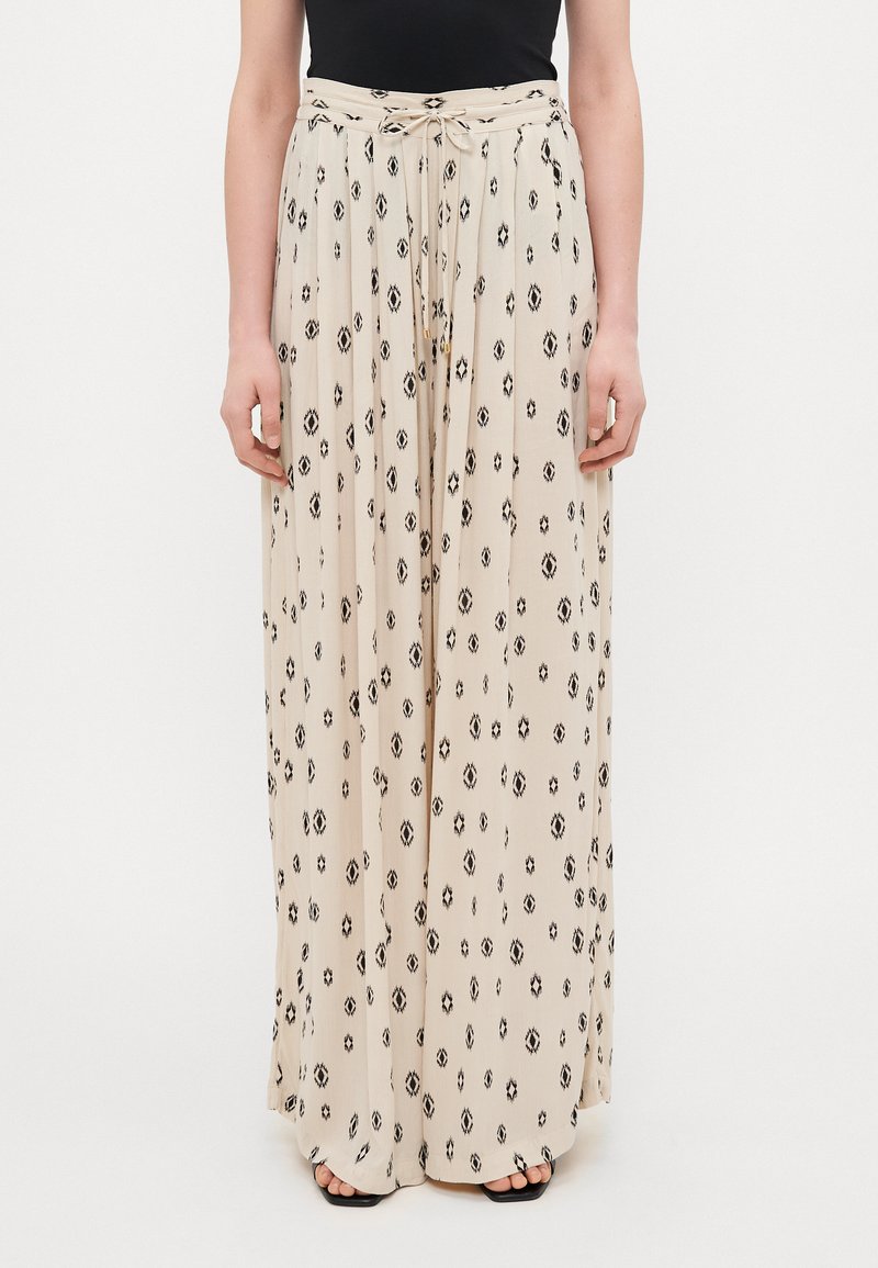 Maxi skirt in beige fabric with black diamond patterns, featuring a tie waistband and pleated design. Smooth texture and flowy silhouette.