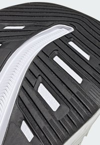 Black rubber shoe sole featuring a textured surface with grooves, white accents, and rectangular cutouts for traction and flexibility.