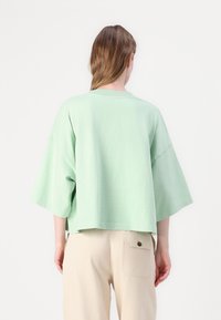 Mint zelena skraćena majica s spuštenim rukavima, izrađena od mekanog pamuka. Ima okrugli izrez i ležeran kroj. Uparena s bež hlačama.