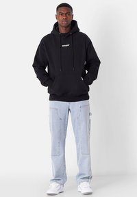 Sudadera de algodón negra con un logo central, mangas largas y un bolsillo tipo canguro, combinada con pantalones cargo azul claro que cuentan con múltiples bolsillos.