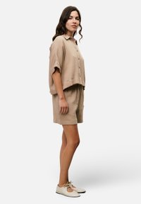 Light beige short-sleeve button-up shirt and matching shorts, using textured fabric. Pairing with cream lace-up shoes. Simple, casual design.