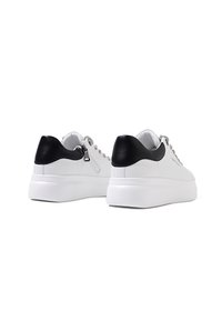 Sneakers bianche con un accento in pelle nera sul tallone, occhielli argentati e una suola spessa bianca. Presentano una chiusura con zip sul retro per un facile indossamento.
