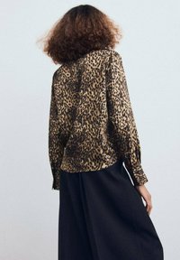 Blusa de leopardo con acabado satinado, mangas largas y corte relajado, combinada con pantalones anchos negros. Patrón animal texturizado visible.