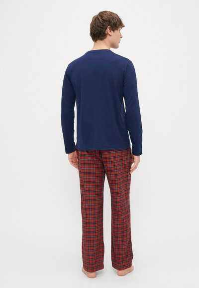T-shirt de manga longa azul-marinho combinado com calças de pijama vermelhas com padrão de xadrez. O tecido parece suave, com um corte descontraído e sem hardware visível.