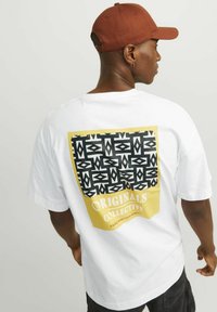 T-shirt bianca con una grafica geometrica nera e testo dorato sul retro, con una vestibilità comoda e maniche corte.