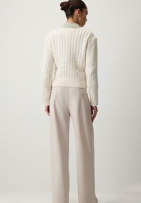 Kermanaitoe spolu kremi za svjetlozelenim ovratnikom, dugim rukavima, rebrastim manžetama i rubom. Upareno sa širokim kremastim hlačama.