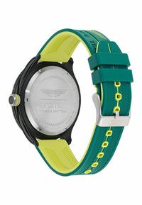 Černé a stříbrné hodinky s černým a stříbrným zadním krytem, zelený a žlutý silikonový pásek s texturovaným vzorem. Obsahuje logo a stříbrnou sponu, sportovní design.