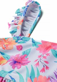 Wielokolorowy strój kąpielowy w kwiaty z falbanowym ramiączkiem, wykonany z gładkiego materiału. Dominującymi kolorami są różowy, pomarańczowy i zielony na białym tle.