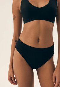 Czarny zestaw bielizny z bezszwowej, miękkiej tkaniny, z wysokim stanem majtek, zapewniający umiarkowane zakrycie i gładką sylwetkę.