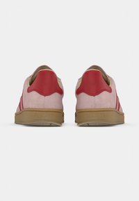 Sneaker in suede rosa con accenti rossi e tre strisce, caratterizzate da suola in gomma strutturata e design del tallone smerlato.