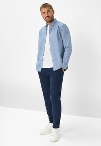 Camicia a quadri blu con collo button-down, indossata sopra una t-shirt bianca, abbinata a chinos blu navy e sneakers bianche.