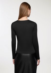 Czarny, długi top z długim rękawem, wykonany z gładkiego materiału, posiada okrągły dekolt i dopasowany krój, noszony z błyszcząca czarną spódnicą.