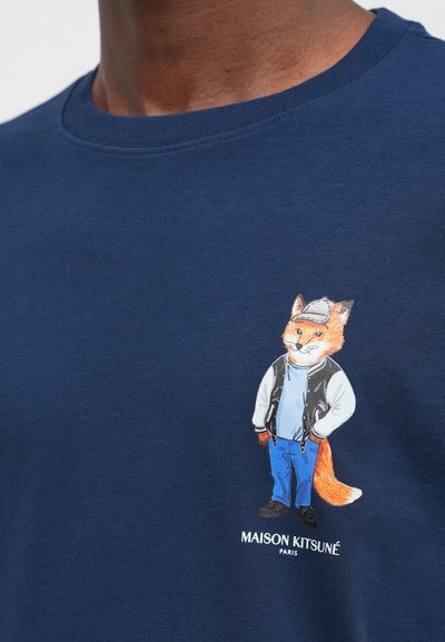 Tumši zils kokvilnas T-krekls ar krāsainu lapsas ilustrāciju, kas tērpta ikdienas apģērbā, ar tekstu "MAISON KITSUNÉ PARIS" apakšā.