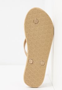 Tan flip-flop sole with textured grip pattern and two round buttons. Flexible, rubber-like material with a smooth finish.