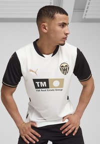 Valge ja must lühikeste varrukatega jalgpallisärk kuldsete aktsentidega. Esiküljel on Valencia CF logo ja sponsori logo.