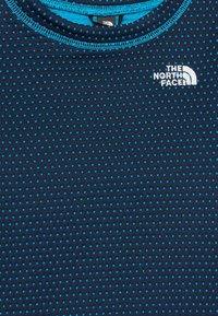 Mornarski t-shirt iz blaga z majhnimi turkiznimi pikami, krožen ovratnik in beli logo "The North Face". Strojno šivanje okoli ovratnika.
