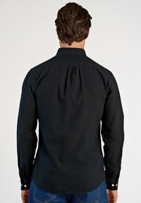 Schwarzes Langarmhemd aus strukturiertem Stoff mit klassischem Kragen, Knöpfen an den Manschetten und abgerundetem Saum. Rückansicht dargestellt.