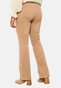 Beige kordfløyelsbukser med vid ben design, med två bakfickor och en texturerad tyg. Bärs med beige klackboots.