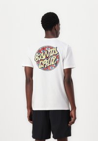 White cotton T-shirt featuring a colorful "Santa Cruz" graphic on the back, with circular pattern and eye designs. Short sleeves, relaxed fit.