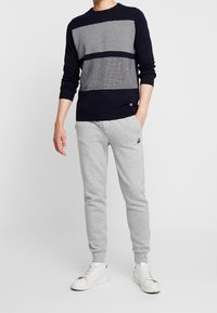Marinblå tröja med ett texturerat horisontellt randmönster, i kombination med ljusgrå sweatpants. Modellen bär vita sneakers.
