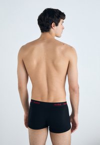 Boxers noirs avec un logo "HUGO" rouge sur la taille, présentés de dos sur un fond neutre, mettant en avant leur design ajusté.