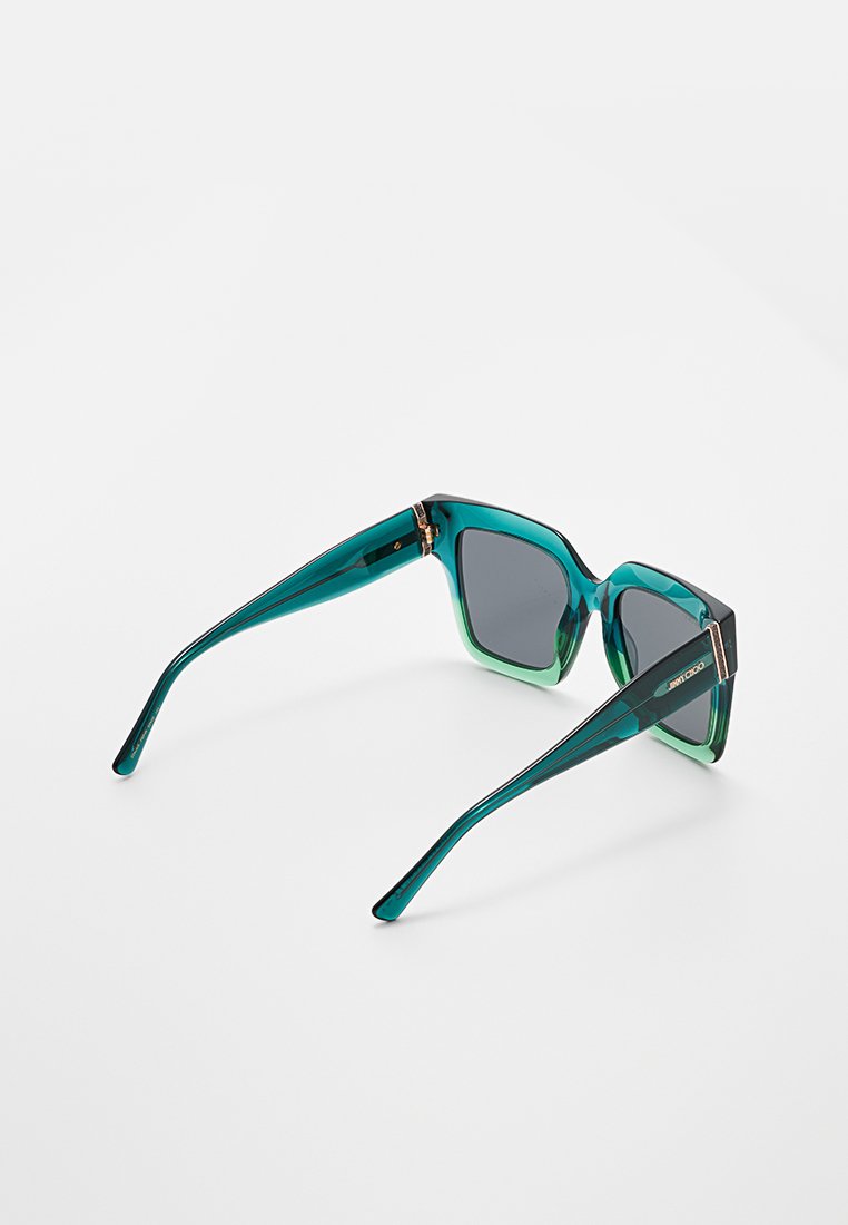 Des lunettes de soleil à monture carrée avec un dégradé de couleurs allant du bleu canard au gris foncé. Elles présentent des branches en plastique lisse et brillant ainsi que des verres teintés foncés.