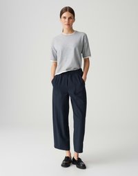 Chemise grise à manches courtes avec des bordures blanches, associée à un pantalon large bleu marine avec un devant plissé et une taille élastique. Mocassins noirs inclus.
