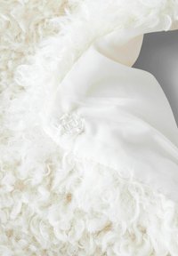 Textuur witte nepleerstof met zachte, krullende vezels, in contrast met een gladde witte stof met een decoratieve knoopdetail.