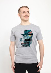 Camiseta de algodón gris con un diseño gráfico colorido de un edificio con acentos en azul, rojo y negro, que incluye patrones y texturas abstractas.