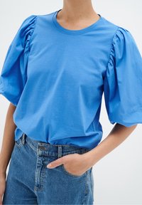 Blå bomullströja med puffärmar, rund halsringning och avslappnad passform, kombinerad med högmidjade denimjeans.