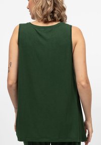 Top senza maniche verde realizzato in morbido cotone. Presenta un collo rotondo, una vestibilità comoda e una texture liscia senza motivi o decorazioni visibili.