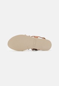 Sandalo in pelle marrone con design a cinturino incrociato e suola beige scanalata, caratterizzato da un logo discreto e una finitura liscia e opaca.