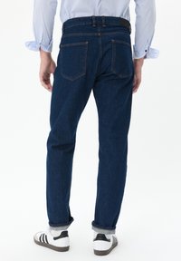 Tumed sinise värvusega teksapüksid otse lõikega, nähtav tikand ja klassikaline viie taskuga disain. Kantud valgete tossudega.