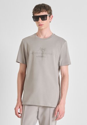 Siva kratki rukav T-shirt s reljefnim logotipom na prsima, napravljen od glatkog materijala, uparen s odvažnim, kutnim crnim naočalama.