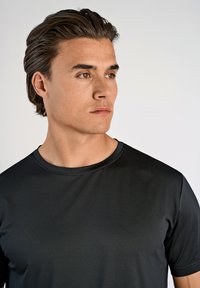 Svart atletisk t-shirt med rund halsringning och korta ärmar, tillverkad av ett mjukt och lätt tyg. Har en subtil textur.