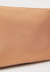 Svetlohnedá vodotesná taška s embosovaným logom "RAINS", hladkým povrchom, jednoduchým dizajnom a bezšvovými okrajmi. Kompaktnej veľkosti, ideálna na cestovanie.