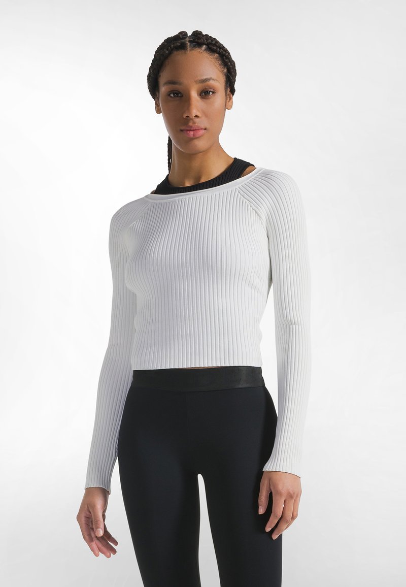 Weißes, geripptes Langarmshirt mit rundem Ausschnitt und schwarzen Akzenten, kombiniert mit schwarzen, hochtaillierten Leggings mit glatter Textur.