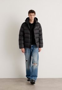 Black puffer jacket with a hood, featuring a quilted design. Paired with light blue jeans that have distressed details and black shoes.