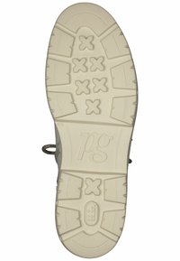 Semelle de sneaker de couleur claire avec un motif texturé, comportant un logo central, des crampons de traction et une boucle pour sécuriser les lacets.