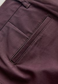 Material bordeaux cu o textură netedă, are o buzunar cu șanț cu cusături curate și linii diagonale subtile care creează o apariție structurată.