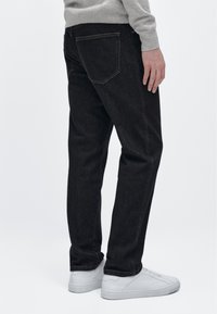 Jeans in denim scuro con taglio dritto, dotati di tasche posteriori e una trama sottile. Abbinati a sneaker bianche.