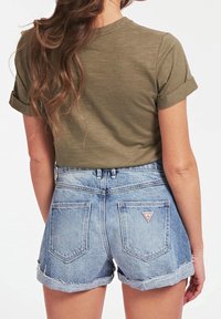 Oliven grøn kortærmet top med optrullede manchetter, parret med lyseblå denim shorts med frynset kant og baglommer.